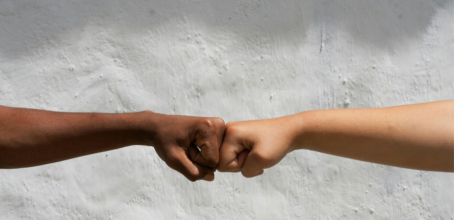 Close up of two arms with different skin tones engaged in a 'fist pump'
