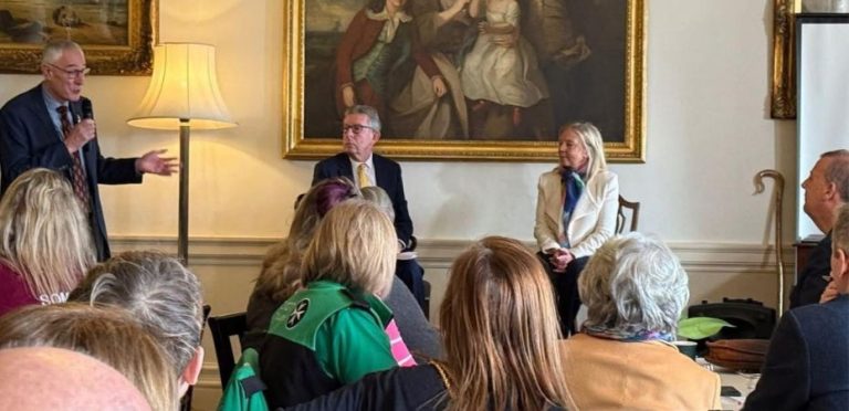 Photograph of attendees at an event, backs to the camera, looking at the speakers