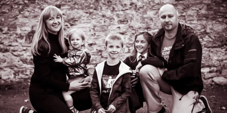 A black and white photo of Joanna (left) with her family. They're smiling at the camera.