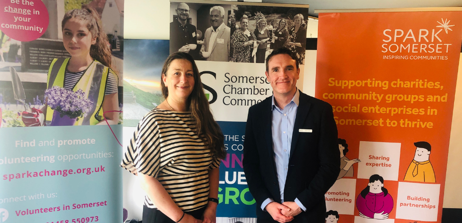 Photograph of Katherine Nolan, CEO of Spark Somerset and David Crew, CEO of Somerset Chamber of Commerce. They are smiling at the camera and standing in front of Spark Somerset, Spark a Change and Somerset Chamber banners.