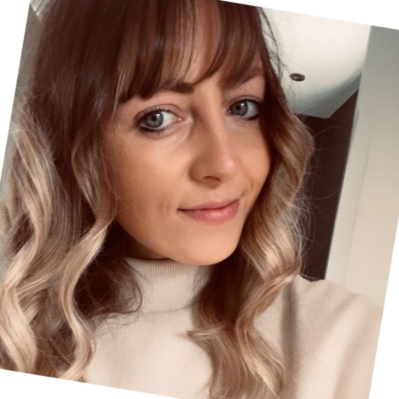 A headshot of Rose Firth; she has curled hair and is wearing a pale-coloured high neck jumper.