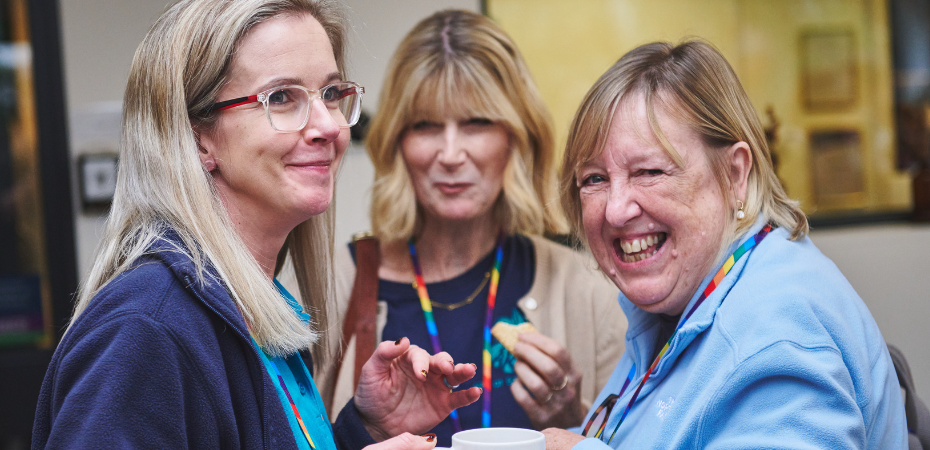 Photograph of three women in conversation, one smiling and looking at the camera.
