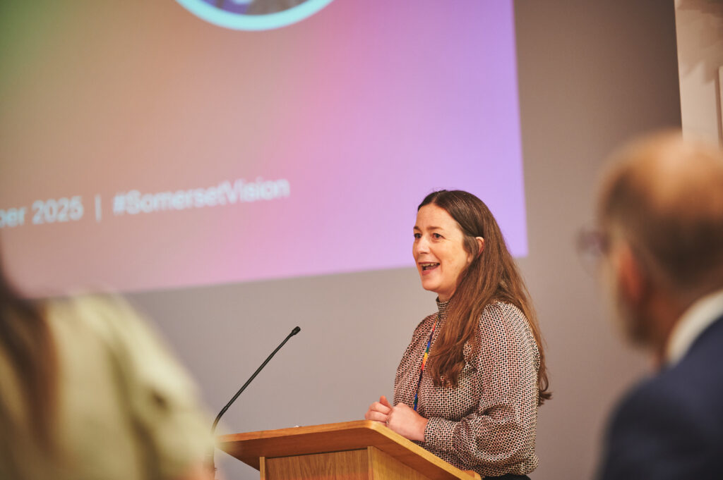 Katherine Nolan delivering her speech on stage, large presentation displayed behind her.
