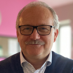 A headshot of Andrew Pattie, a man with glasses and a moustache.