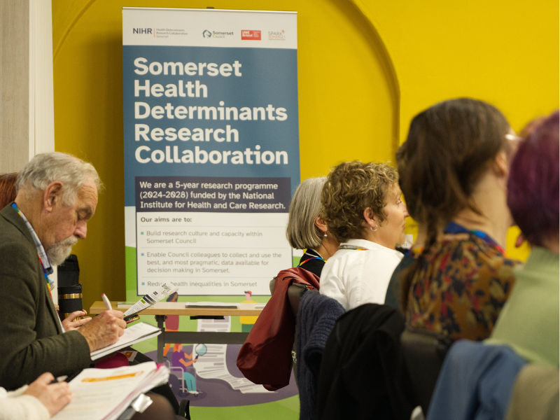 Photograph of an HDRC banner sign displayed at an event with attendees in the foreground.