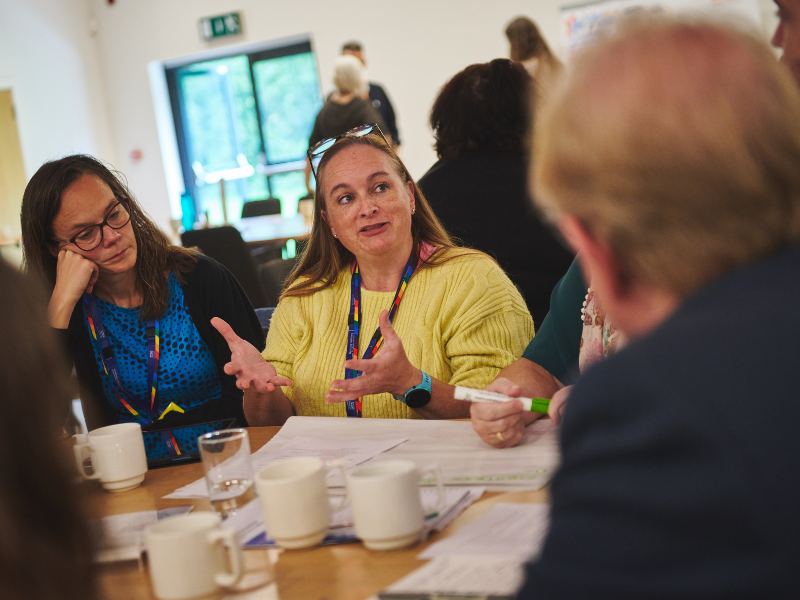 A photograph of a group of people sat at a table having a discussion at a conference.