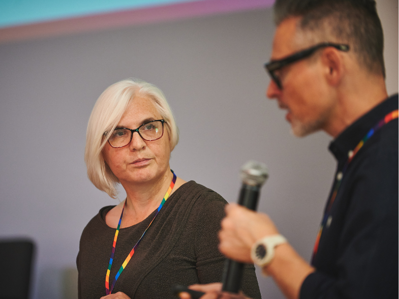 A photograph of woman looking at a man who is talking into a microphone.