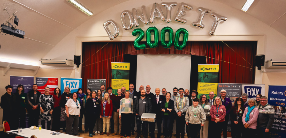 Photograph of a larger group of attendees at the Donate IT Celebration event. They are smiling at the camera. Behind them are helium balloons spelling out 'Donate T 2000'.