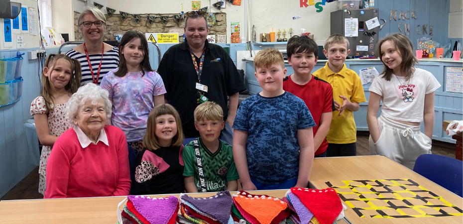 A photo of a group of children and adults standing together and smiling at the camera. There is a table covered in colourful bunting in the foreground.