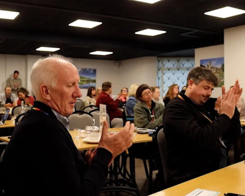 An image from a Somerset Youth Alliance event of people sat at tables and clapping