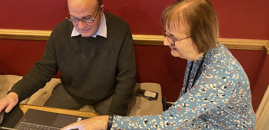 Lynne and John, who are featured in the case study, sitting at a table together looking at a laptop and smiling.