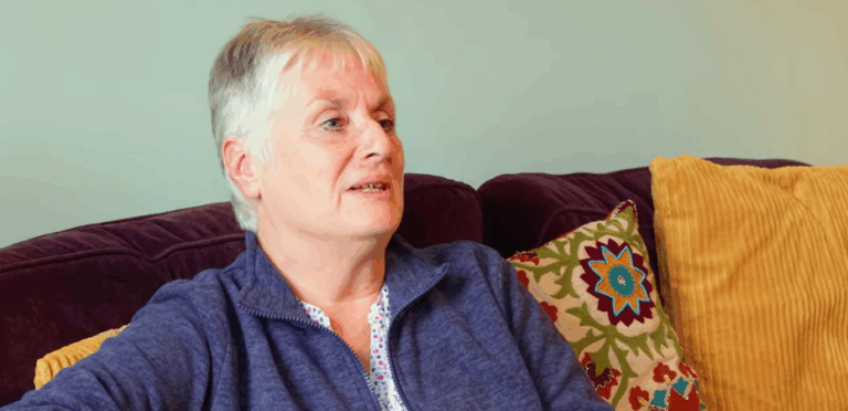 Image of Sue Crisfield, sat on a sofa, in conversation with someone off camera