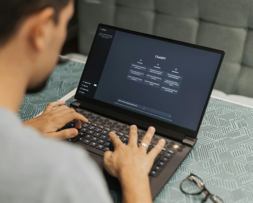 An over-the-shoulder image of a young man on his laptop, using Chat GPT