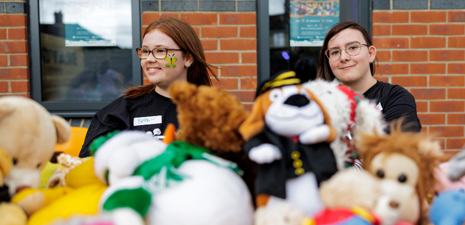 Two young women standing behind a table covered in soft toys