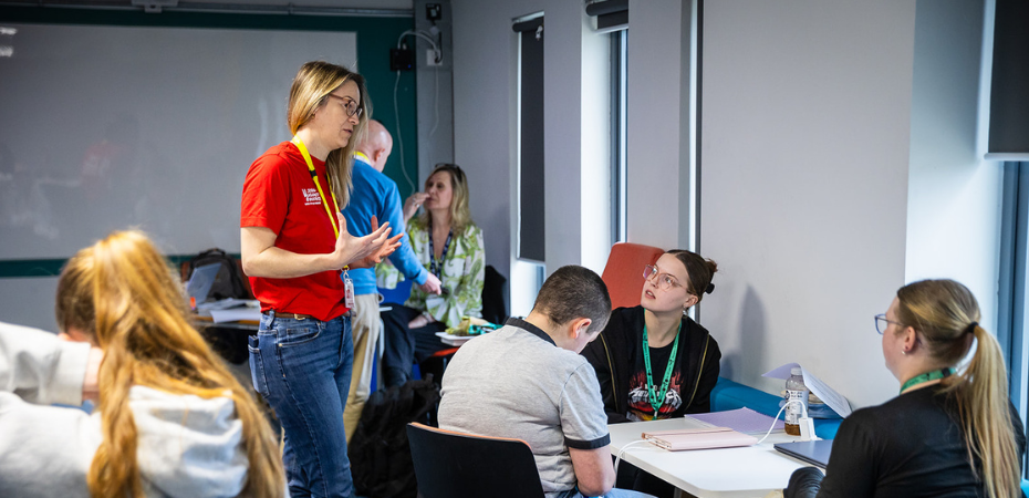 A photo of a blonde woman in a red, Stand Against Violence t-shirt, engaging with learners at a training session