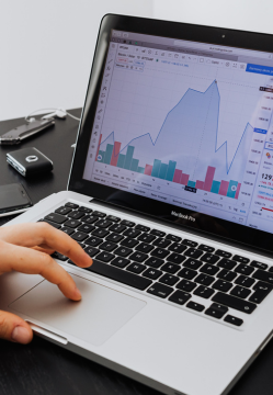 Photograph of a laptop with charts on the monitor and someone's hand on the keyboard