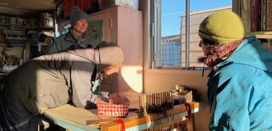 A photo of a group of people in a rustic shed, wrapped up in scarves and wooly hats.