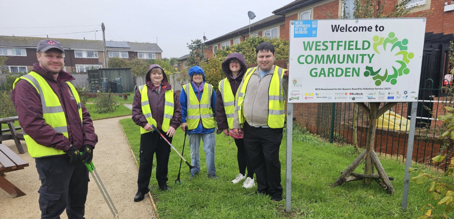 Westfield volunteers wearing high-vis jackets and wet weather gear posing next to a sign for Westfield Community Garden