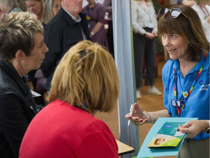 Photograph of three women in conversation. One of them is wearing an Alzheimer's UK t-shirt.