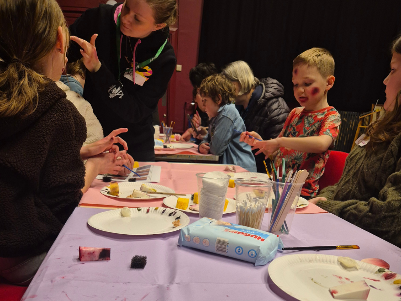 Photograph of children taking part in an art activity around a table supervised by an adult volunteer