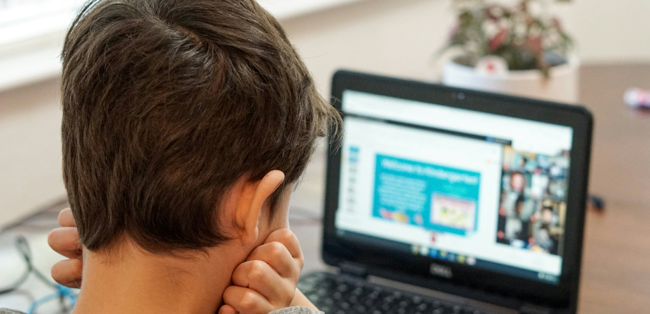 Photograph of a young boy using a laptop, the camera is looking over his shoulder at the screen from behind.