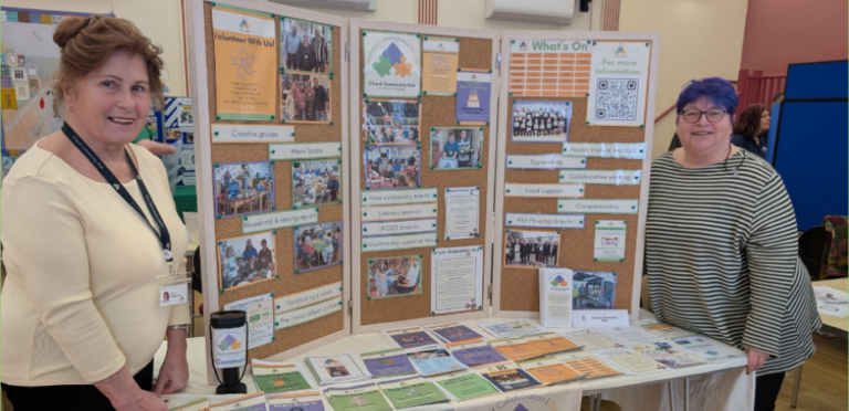 Photo of two smiling women standing next to a display board at an event