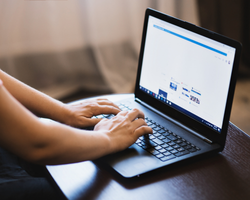 Image showing a cropped-in image of a person using a laptop. Facebook is open on the screen.