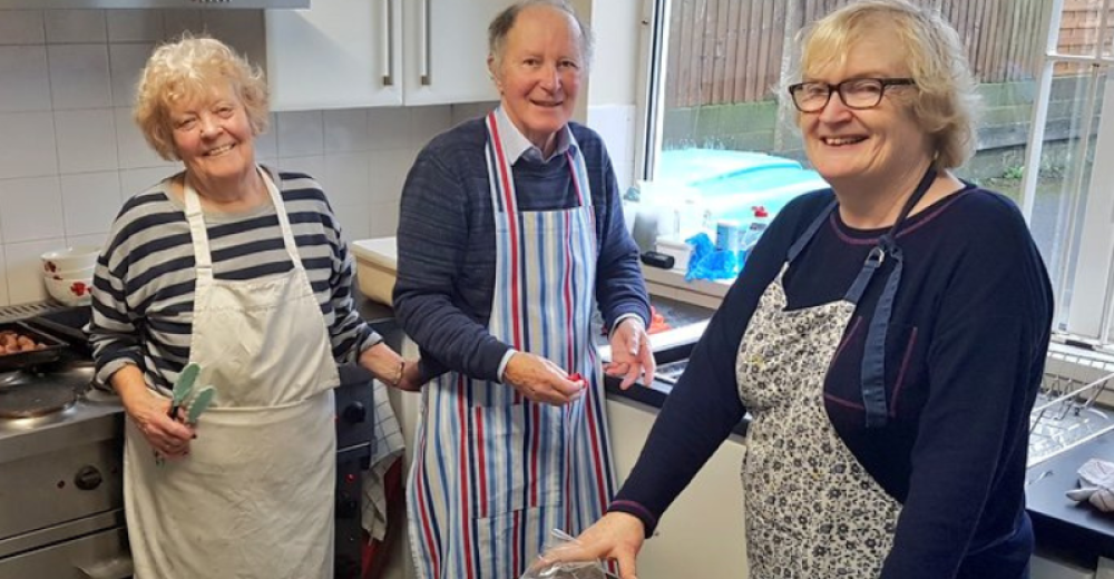 Three people volunteering in a kitchen, smiling at camera