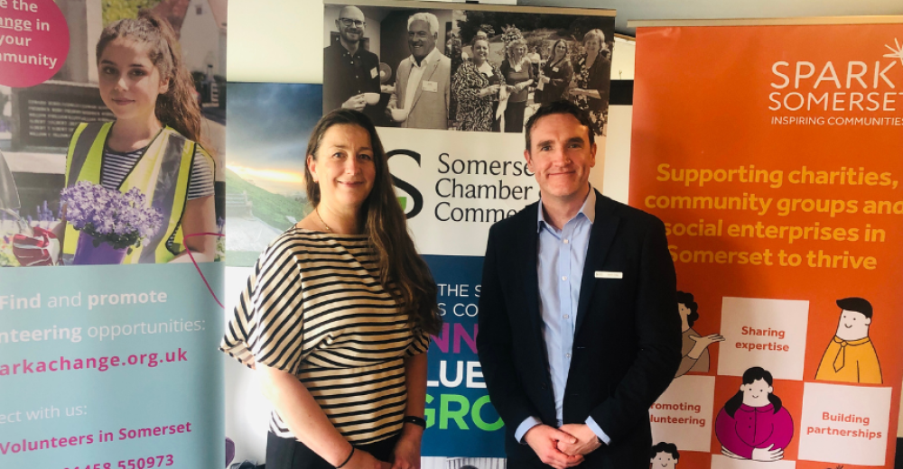 Photograph of Katherine Nolan, CEO of Spark Somerset and David Crew, CEO of Somerset Chamber of Commerce. They are smiling at the camera and standing in front of Spark Somerset, Spark a Change and Somerset Chamber banners.
