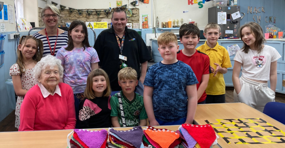 A photo of a group of children and adults standing together and smiling at the camera. There is a table covered in colourful bunting in the foreground.