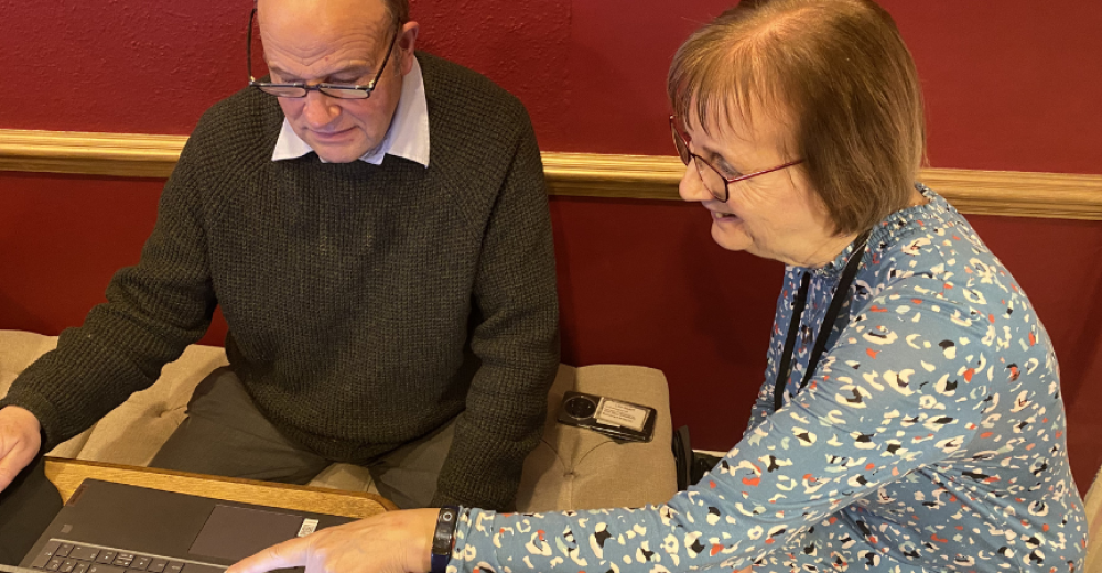 Lynne and John, who are featured in the case study, sitting at a table together looking at a laptop and smiling.