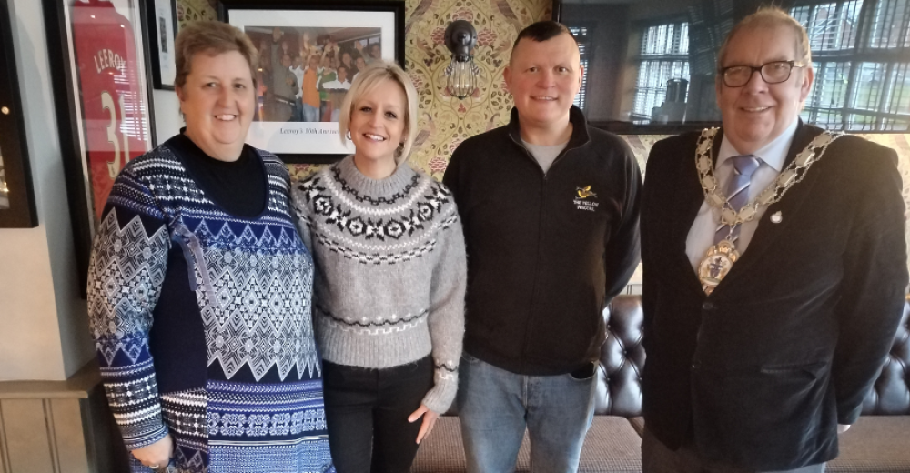 A photograph of four people stood in a row smiling at the camera, one is the mayor