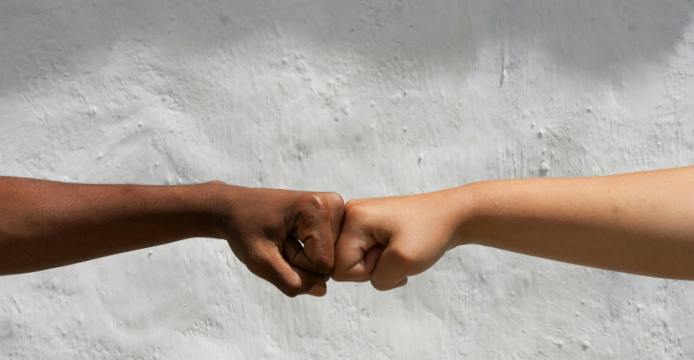 Close up of two arms with different skin tones engaged in a 'fist pump'