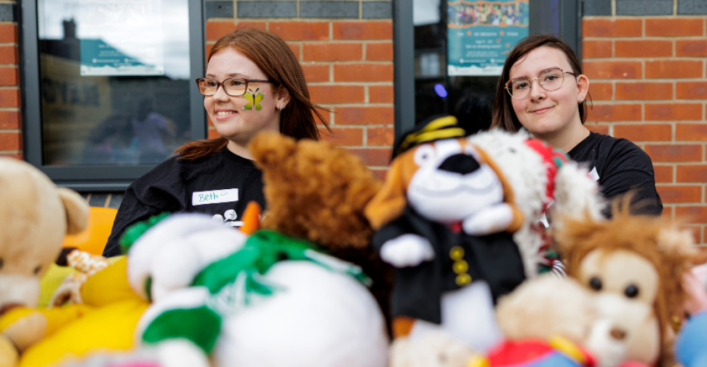 Two young women standing behind a table covered in soft toys