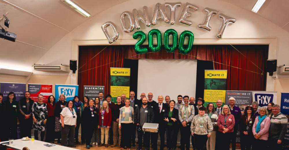 Photograph of a larger group of attendees at the Donate IT Celebration event. They are smiling at the camera. Behind them are helium balloons spelling out 'Donate T 2000'.