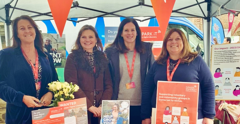 Photograph of four member of the Spark Somerset team standing at a Spark Somerset branded stall at an outdoor event.