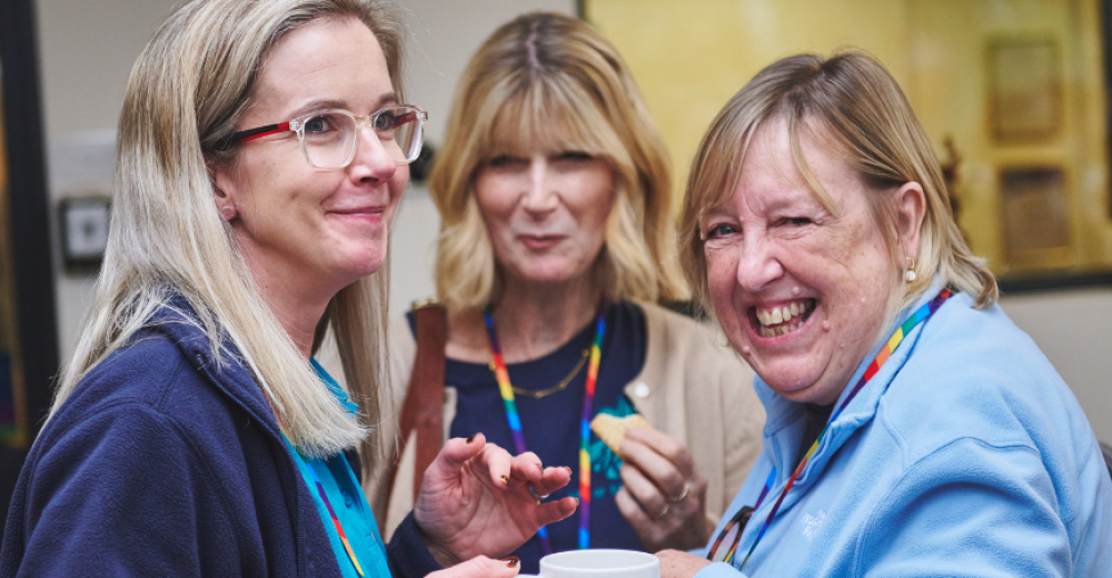 Photograph of three women in conversation, one smiling and looking at the camera.