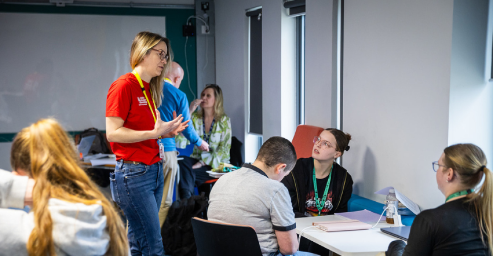 A photo of a blonde woman in a red, Stand Against Violence t-shirt, engaging with learners at a training session
