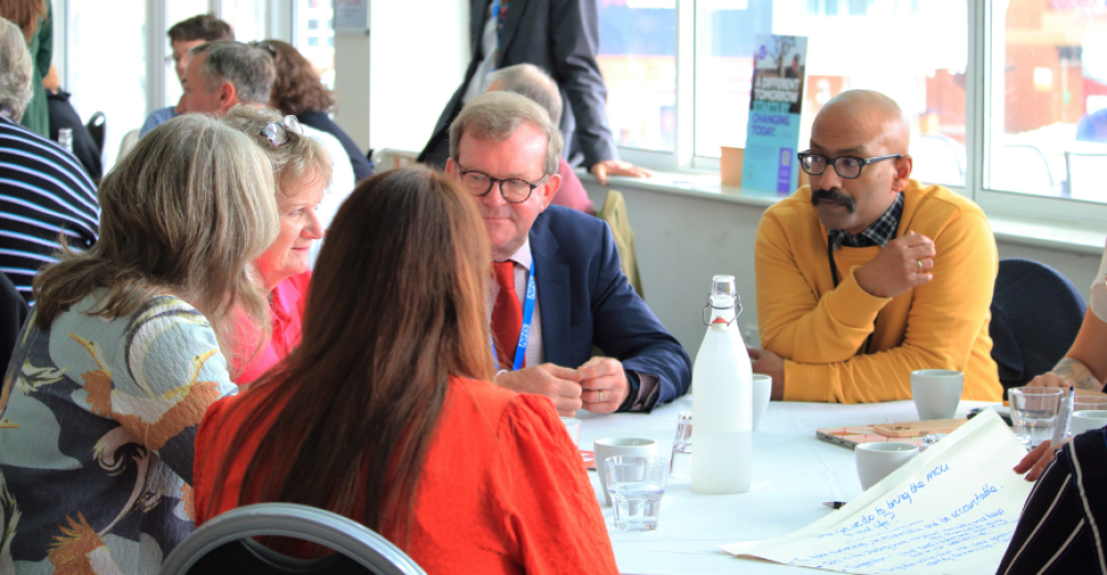 Photograph of a group of people sat at a table having a discussion in a conference setting