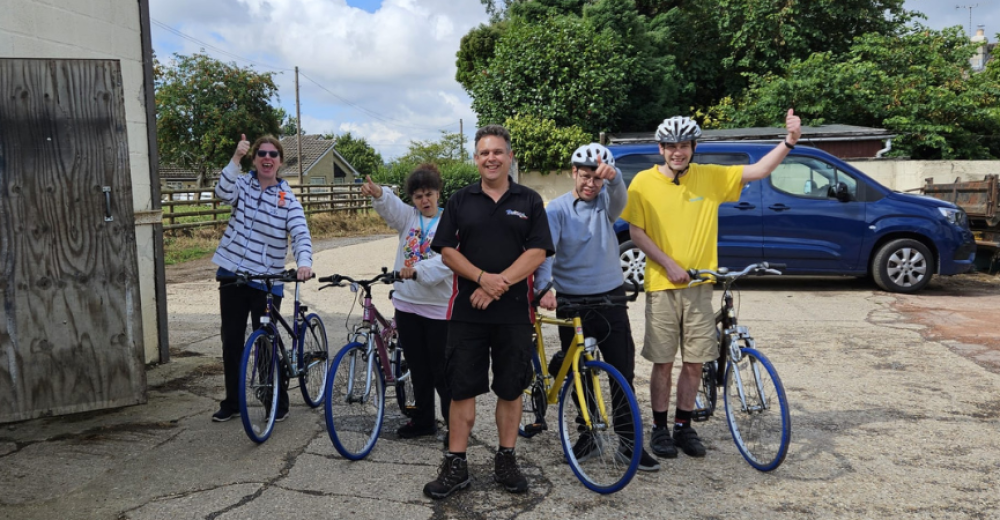 A group of people posing with bicycles. They are looking at the camera and smiling.