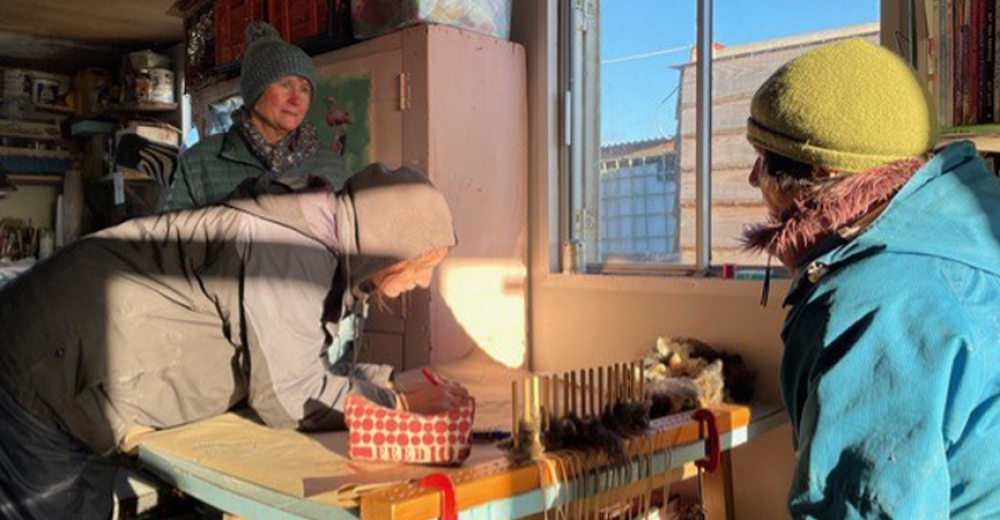 A photo of a group of people in a rustic shed, wrapped up in scarves and wooly hats.