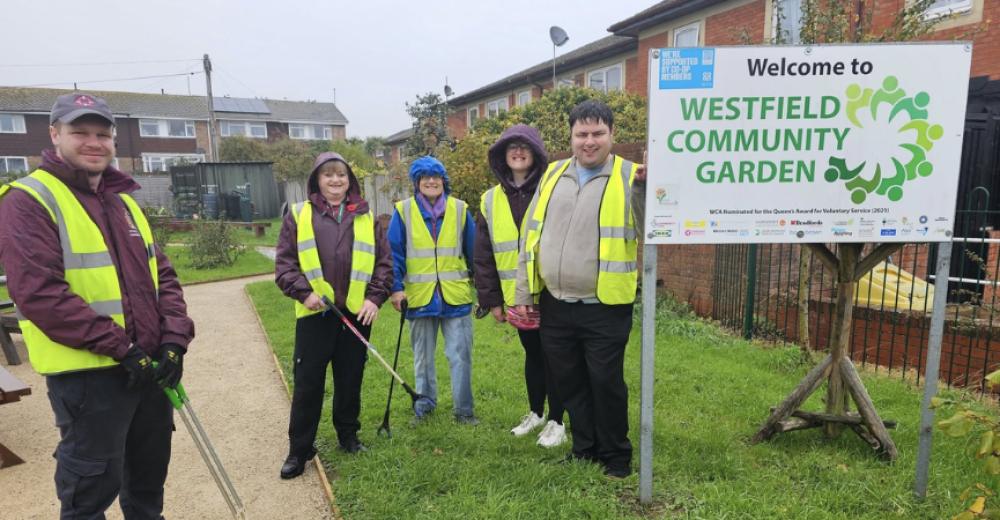Westfield volunteers wearing high-vis jackets and wet weather gear posing next to a sign for Westfield Community Garden